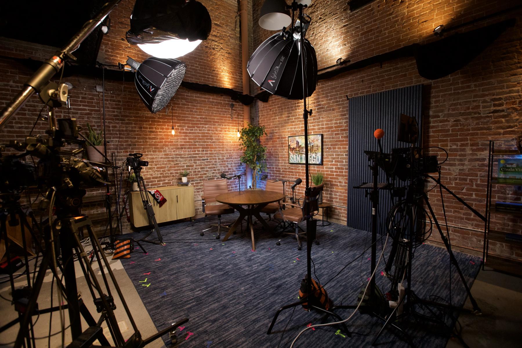 The DIA Live Studio set from the camera line: brick wall, softboxes overhead, round table, and slat wall lit and ready to record